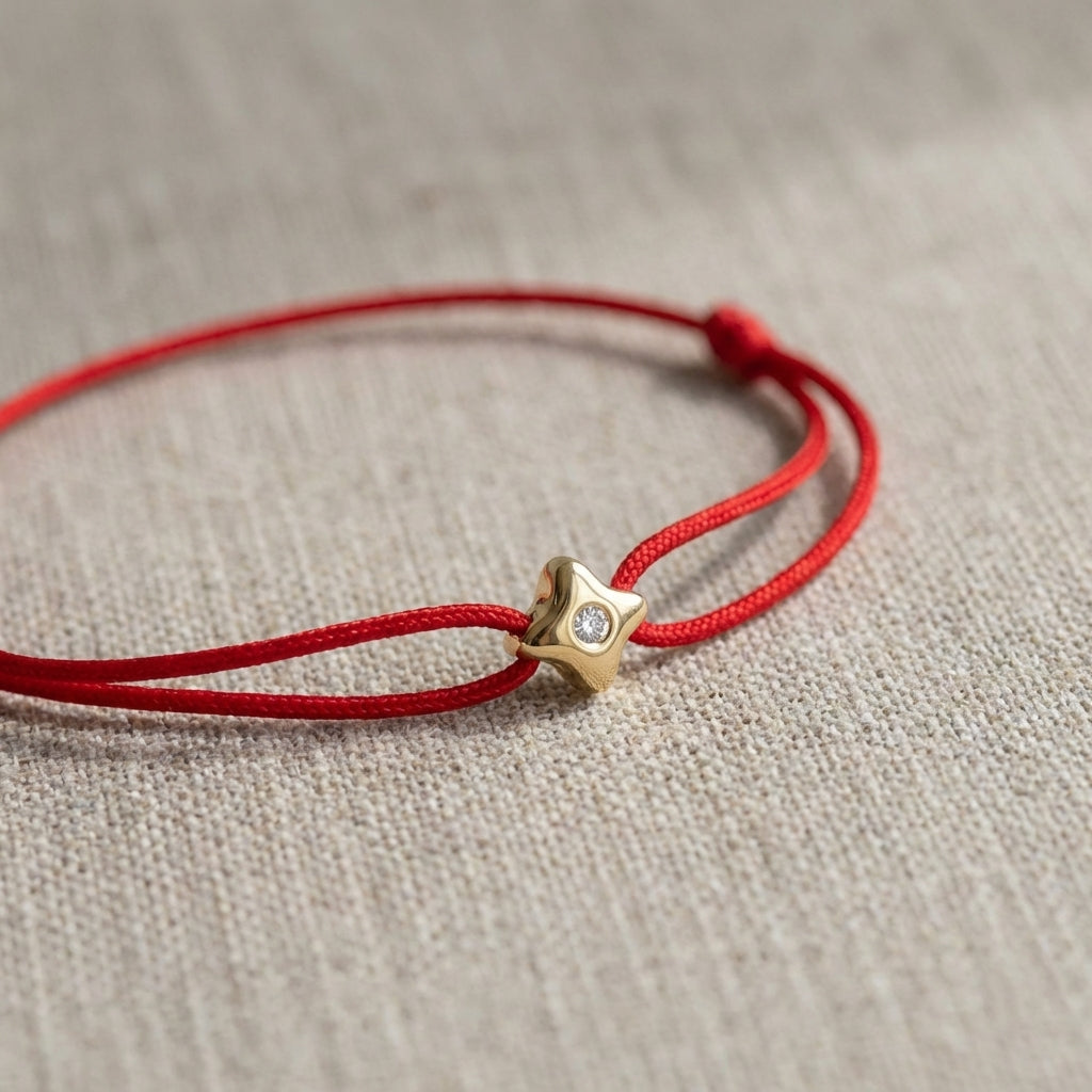 Close-up of North Star bracelet with diamond and red cord on neutral fabric, natural daylight with soft shadows.